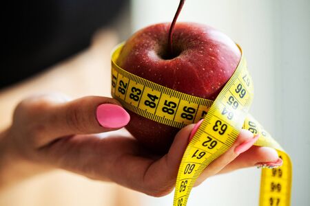 Diet concept. Apple with measure tape in female hand