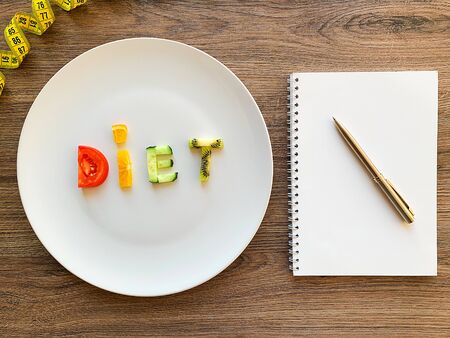 Word DIET made of sliced vegetables in white plate and diet plan on wood backgroundの写真素材