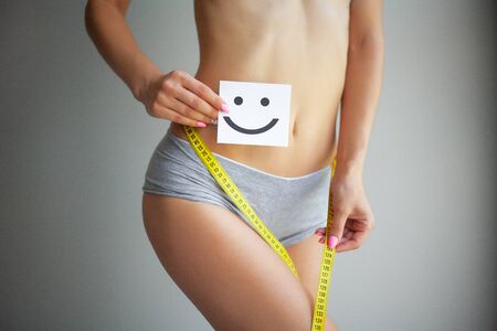 Women Health. Closeup Of Healthy Female With Beautiful Fit Slim Body In White Panties Holding White Card With Happy Smiley Face In Hands. Stomach Health And Good Digestion Concepts. High Resolutionの写真素材