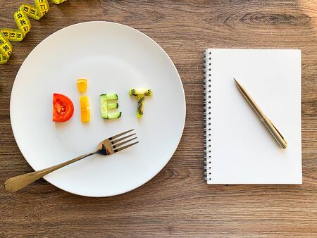 Word DIET made of sliced vegetables in white plate and diet plan on wood backgroundの写真素材