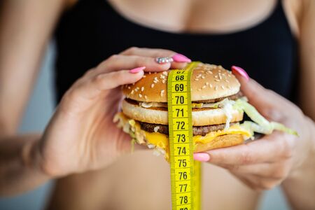 Harmful food. The choice between malicious food and sport. Beautiful young girl on a diet. The concept of beauty and health. On a gray backgroundの写真素材