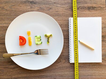 Word DIET made of sliced vegetables in white plate and diet plan on wood backgroundの写真素材