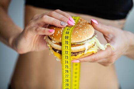 Harmful food. The choice between malicious food and sport. Beautiful young girl on a diet. The concept of beauty and health. On a gray backgroundの写真素材