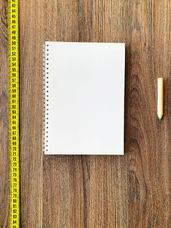 Diet concept. Measuring tape on wooden background with book diary notepad and pen for healthy fitness backgroundの写真素材