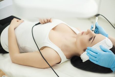Doctor with Ultrasonic scraber. Doing procedure of ultrasonic cleaning of face. Model, profile. Cosmetological clinic. Patient. Healthcare, clinic, cosmetology.の写真素材