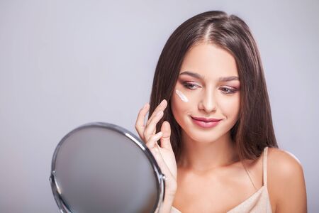 Beauty Face. Closeup Of Sexy Young Woman With Concealer Brush And Mirror In Hands. Portrait Of Beautiful Healthy Female Model Applying Concealer Under Eyes. Skin Cosmetics. High Resolutionの写真素材