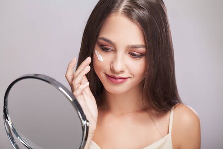 Woman with healthy face applying cosmetic cream under the eyesの写真素材