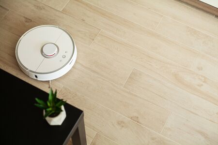 Smart House. Vacuum cleaner robot runs on wood floor in a living roomの写真素材