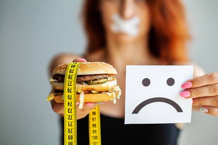 Diet. Portrait woman wants to eat a Burger but stuck skochem mouth, the concept of diet, junk food, willpower in nutritionの写真素材