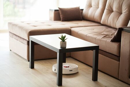 Smart House. Vacuum cleaner robot runs on wood floor in a living room.の写真素材