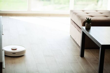 Smart House. Vacuum cleaner robot runs on wood floor in a living room.の写真素材