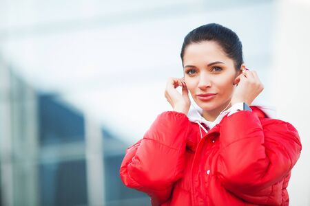 Photo of Joyful Fitness Woman 30s in Sportswear Touching Earpod and Holding Mobile Phone, While Resting in Green Parkの写真素材
