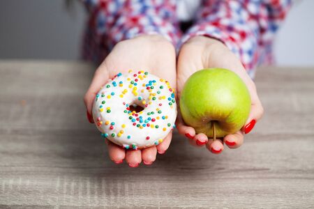 Women is choosing choice between donut and green apple during her dieting session.の写真素材