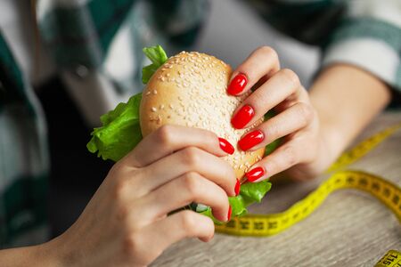Woman with burger and measuring tape while dietingの写真素材