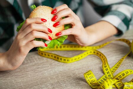 Woman with burger and measuring tape while dietingの写真素材