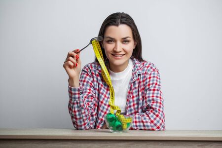 Young pretty woman adheres to diet with measuring tape on white wall backgroundの写真素材