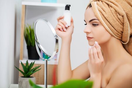 Woman getting ready for work doing morning makeup in bathroom mirror at homeの写真素材