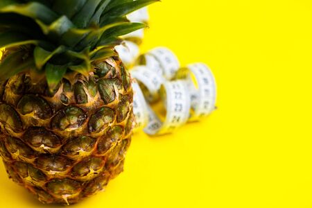 Ripe pineapple with tape measure on a yellow background.