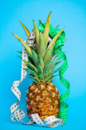 Ripe pineapple with measuring tape on a blue background.