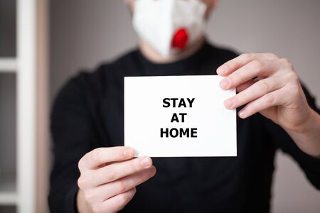 Man in a mask holds a sheet with the inscription stay at homeの写真素材