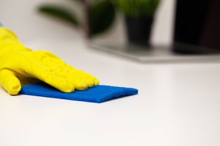 Close up of worker hand wiping dust in office in yellow gloves.