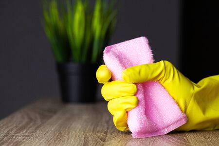 Close up of worker hand wiping dust in office in yellow gloves.