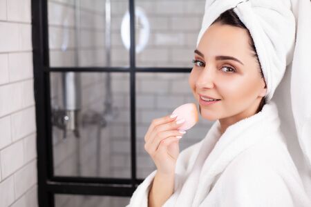 Cute woman in white coat and towel on her head makes herself a makeupの写真素材