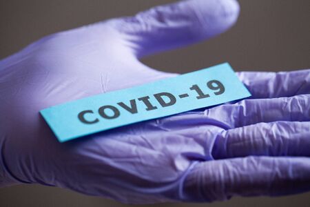 Woman in protective gloves holding inscription coronavirus