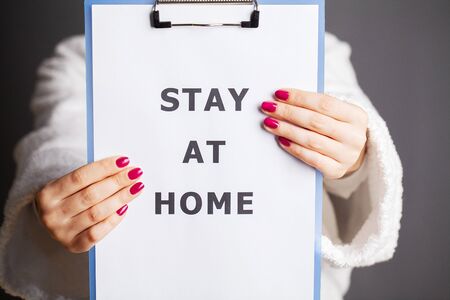 Woman holding blank with inscription stay at home calling for stop spreading covid-19.