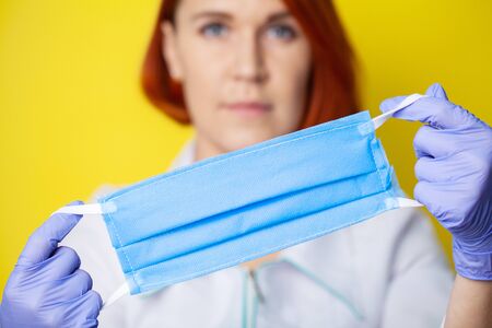 Woman holding mask to cover mouth and nose to protect against virus on yellow background