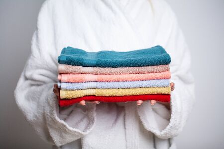 Woman in a white coat holding a stack of colored towelsの写真素材