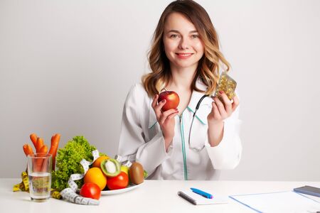 Nutritionist holding omega-3 fish oil vitamin tablet and fresh fruit in her room recording a video blog on her phoneの写真素材