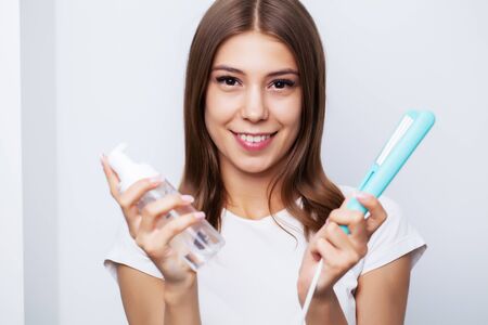 Beautiful young female model takes care of her hair and uses a hair straightenerの写真素材