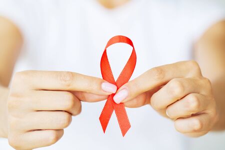 A woman holding a red ribbon emerges from a critical situation after overcoming AIDS.