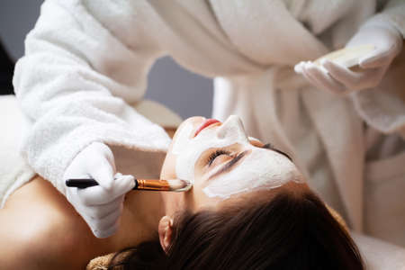 Beautician applies a mask on the face of a woman lying on a couch in a spa.の写真素材