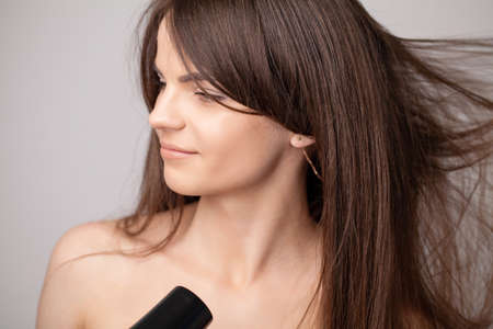 Beautiful smiling woman drying her long hair with dryer