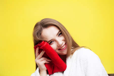 Young woman wiping her face with towel on yellow backgroundの写真素材