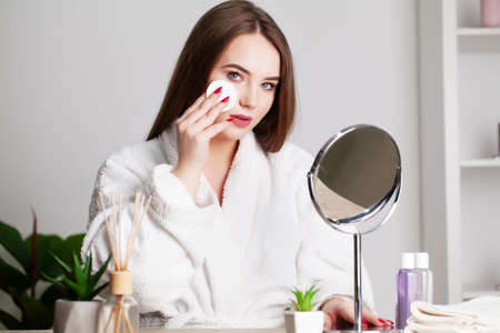 Smiling young woman washing her face with facial cleansing sponge at bathroomの写真素材