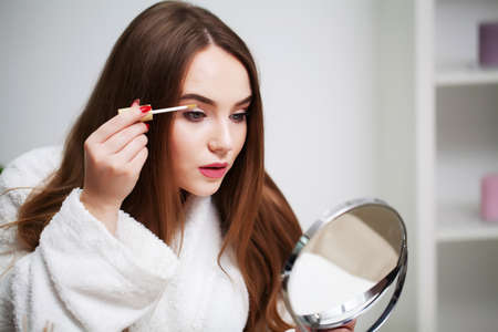 Beautiful woman using brush for daily makeup in bathroomの写真素材