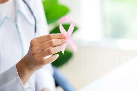 Smiling female doctor with pink cancer awareness ribbon in hospital cabinet.の写真素材