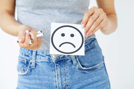 Stop smoking, woman holding broken cigarettes in hands and card with sad smile.の写真素材