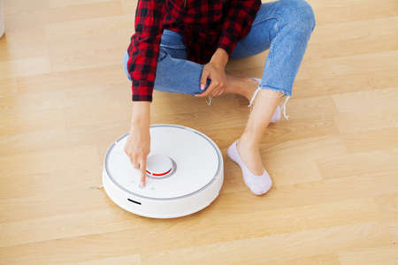 Close up of woman turns on smart robot vacuum cleaner