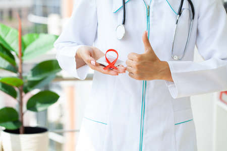 Close Up woman hand holding red ribbon HIV, world AIDS day awareness ribbon.