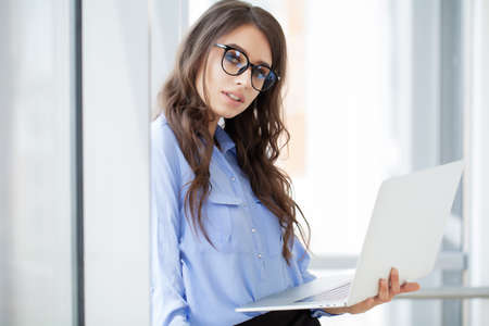 Charming businesswoman near window working on laptop in office