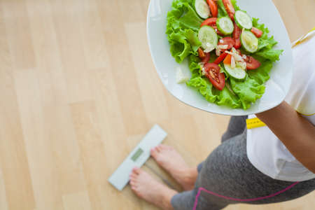 Diet concept, woman holding fresh diet salad measure her weightの写真素材