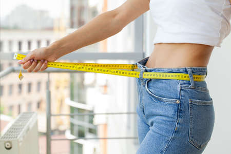 Slender woman in jeans and a white T-shirt measures her waistの写真素材