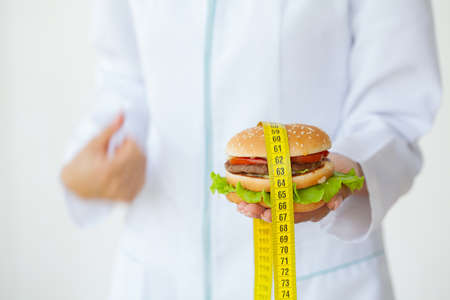 Diet concept, doctor holding harmful fat burger with yellow measuring tapeの写真素材
