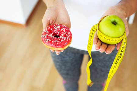 Diet concept, woman holding a choice of harmful donut and fresh apple.の写真素材