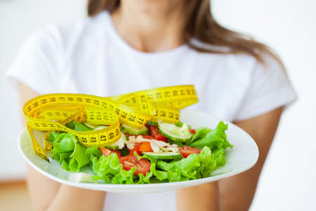 Young woman hold healthy salad with green fresh ingredients and yellow tapeの写真素材