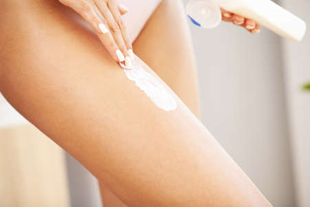 Woman applying body cream on her leg in bedroom, closeupの写真素材